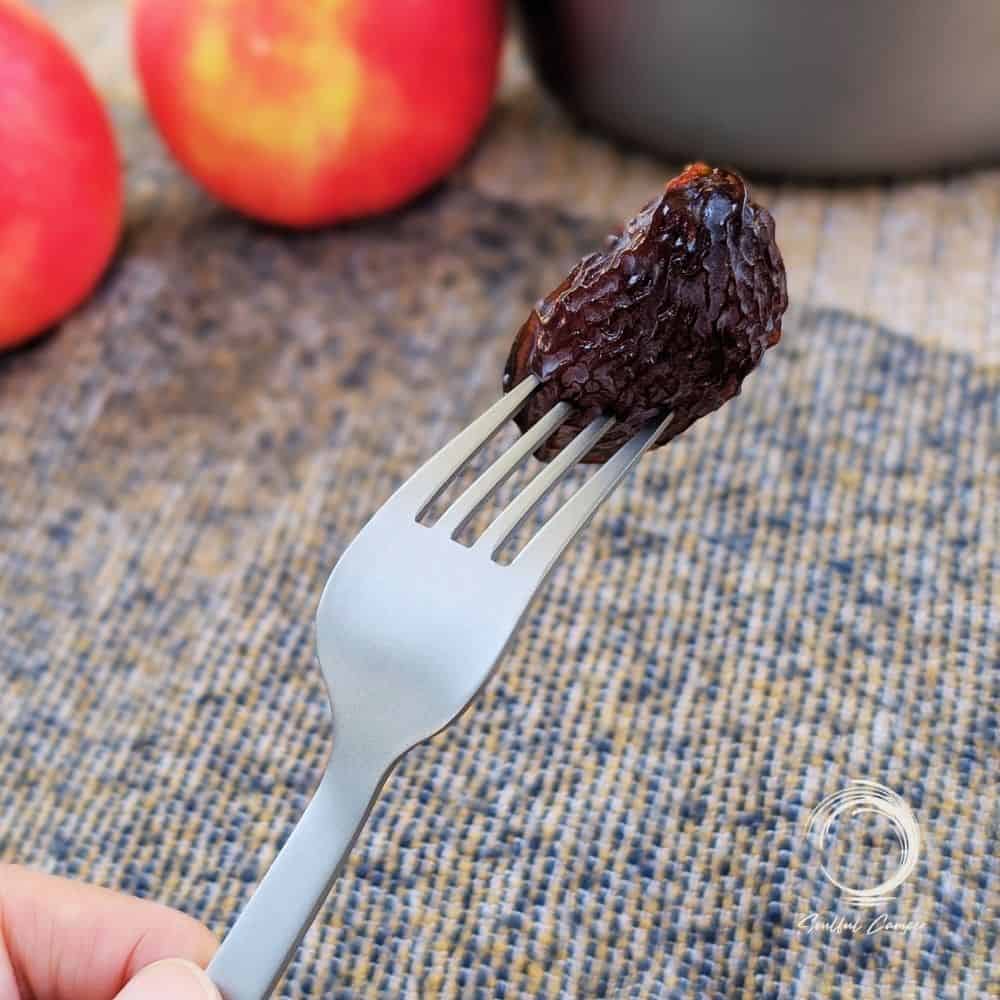 Titanium fork holding a prune, styled with apples in the background