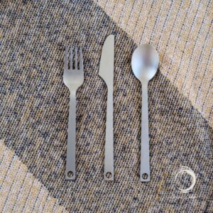 Top-down view of titanium camping cutlery set on a rustic mat