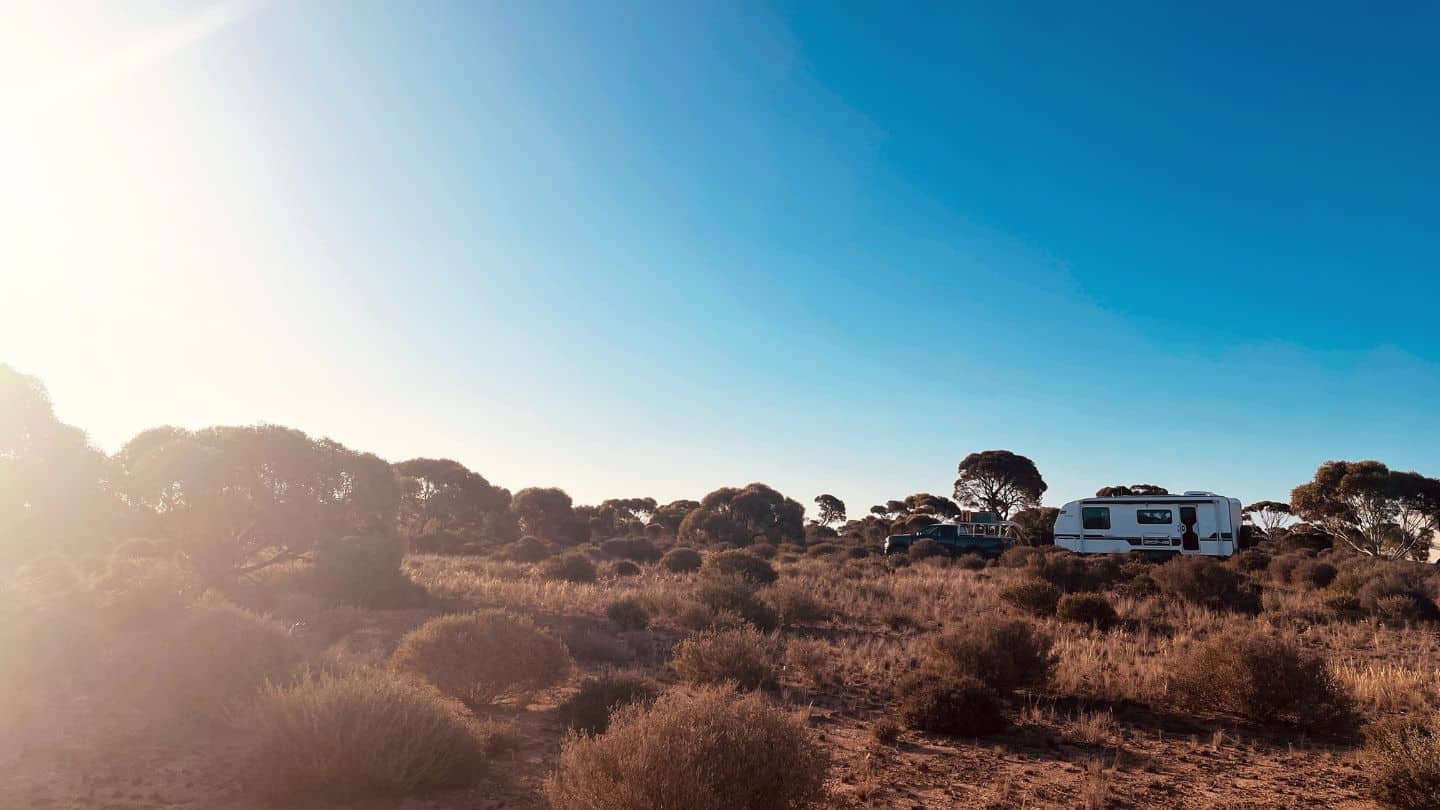 Caravan parked at a roadside camping spot on the Nullarbor Plain surrounded by Australian bushland.