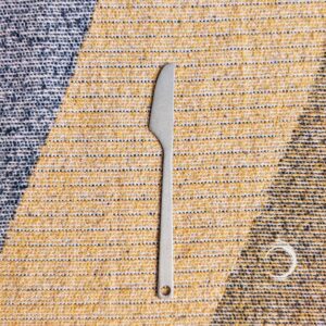 Titanium camping knife with minimalist design on woven outdoor fabric background.