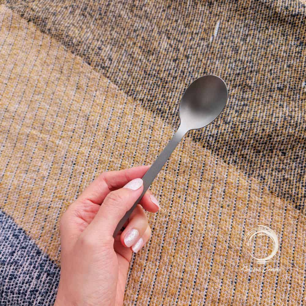 Lightweight Soulful Camper titanium camping spoon held over outdoor picnic mat