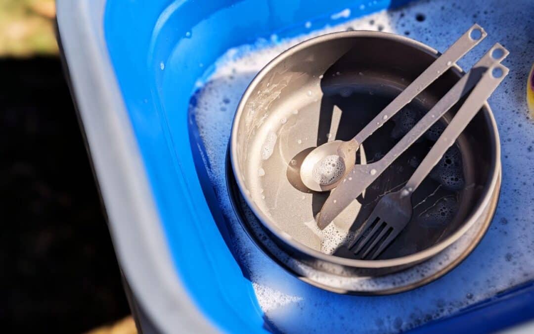 Titanium camping bowl, fork, and spoon being washed in soapy water outdoors – durable and lightweight gear by Soulful Camper